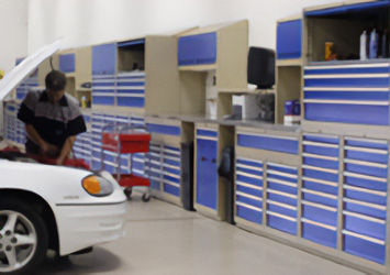 man working on a car engine standing next to a wall of cabinet and shelf storage